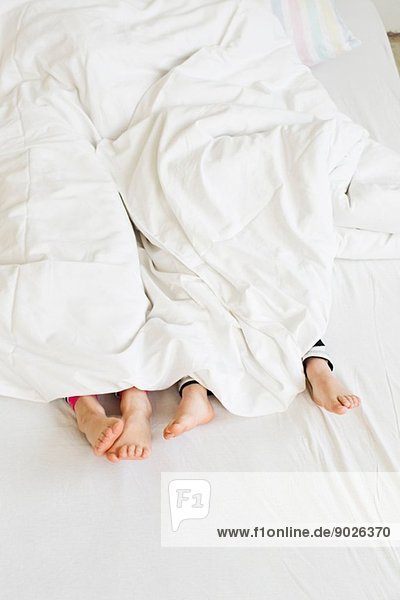 Junge Schwesternfüße aus der Bettdecke auf dem Bett herausragend