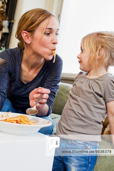 Mittlere erwachsene Mutter  die mit ihrer Tochter Spaghetti isst.