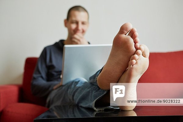 Mid Erwachsene Mann entspannen auf dem Sofa in Laptop vertieft