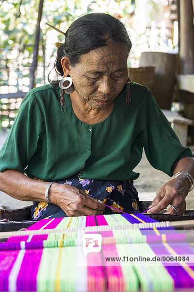 Woman with traditional facial tattoos and ear jewellery from the Chin people  ethnic group  the last of their kind  weaving on a loom  Rakhine State  Myanmar