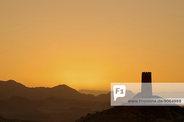 Sonnenaufgang hinter der Silhouette eines einsamen  verfallenden Wachturms am Rande der Wahiba Sands Wüste  Al Mudayrib  asch-Scharqiyya  Oman