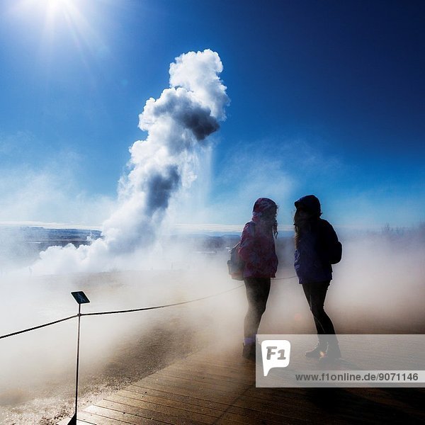 Teenager girls with Strokkur geyser in the background Iceland.