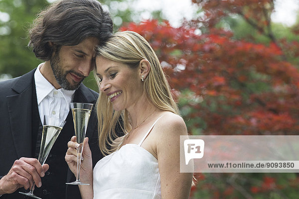 Happy bride and groom with champagne glasses in garden