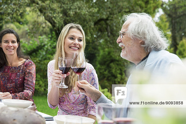 Frau und älterer Mann klirren auf einer Gartenparty mit Weingläsern