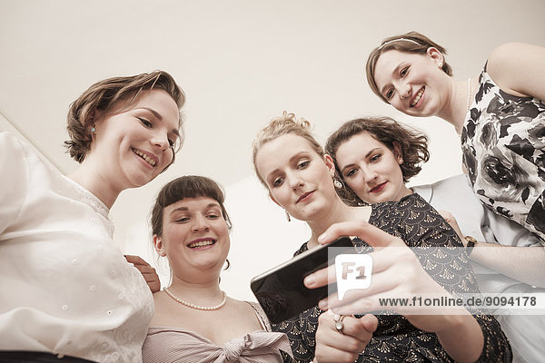 Young women in vintage dresses looking at cell phone