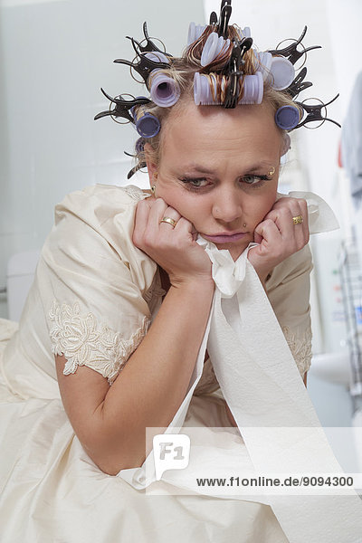 Frustrated bride with curlers sitting on toilet