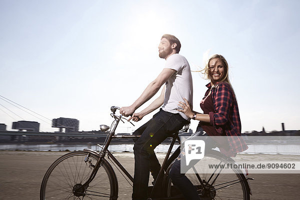 Happy couple riding bicycle on riverbank
