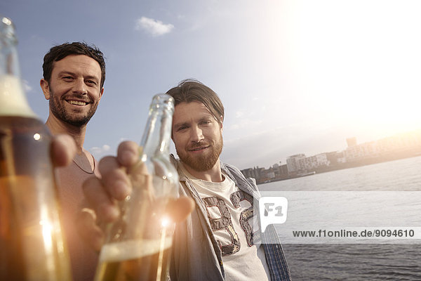 Portrait von zwei Freunden mit Bierflaschen am Flussufer