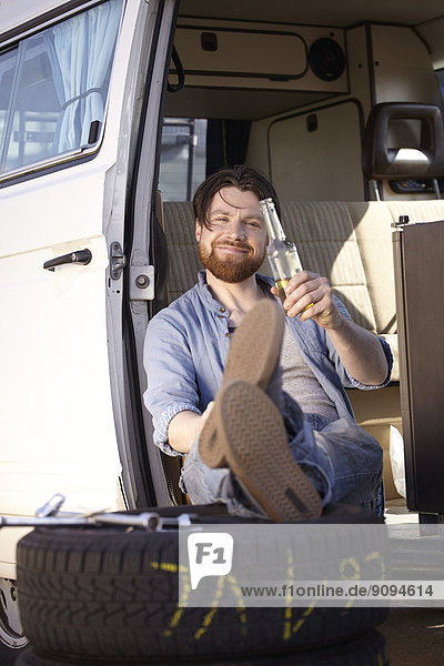 Mann im Auto sitzend mit Reifen und Bierflasche