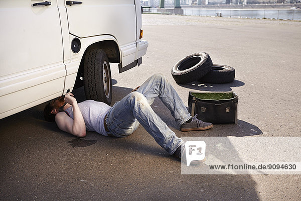 Mann auf dem Boden liegend  Auto reparierend