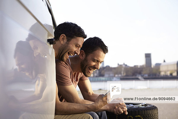 Zwei lachende Männer sitzen im Auto und schauen auf ein digitales Tablett.