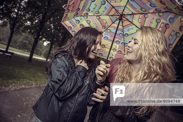 Zwei glückliche junge Frauen unter dem Regenschirm im Park