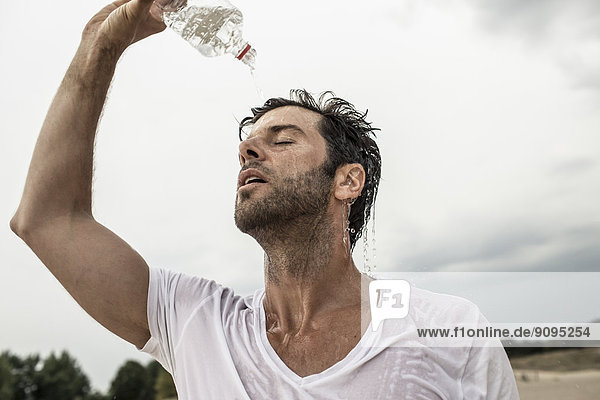 Porträt eines Mannes  der Wasser aus der Flasche über sich gießt.
