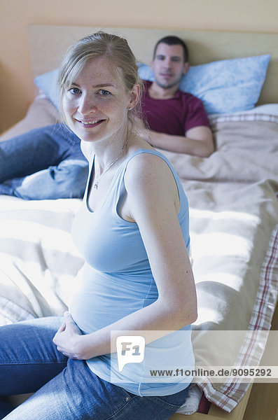 Couple expecting a baby sitting on bed at home
