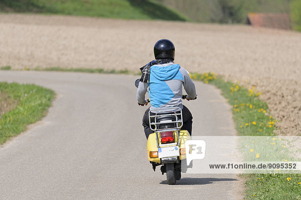 Junger Mann fährt mit seiner Vespa auf der Landstraße