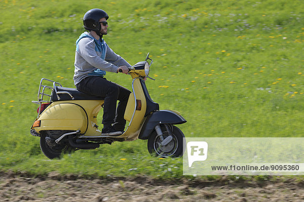 Young man driving with his Vespa on meadow