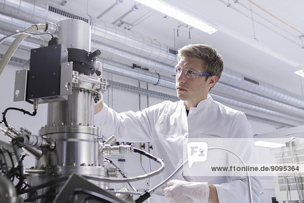 Scientist standing in analytical laboratory with scanning electron microscope and spectrometer
