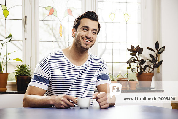 Porträt eines glücklichen jungen Mannes am blauen Tisch mit einer Tasse