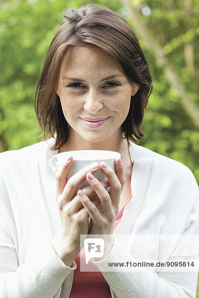 Porträt einer jungen lächelnden Frau mit einer Tasse Kaffee im Garten