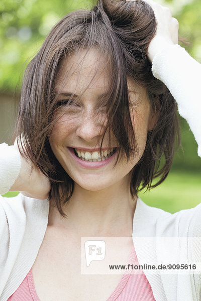 Porträt einer lächelnden jungen Frau mit Händen im Haar