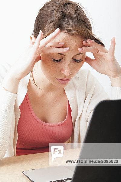 Junge Frau mit Kopfschmerzen zu Hause mit Schreibtischarbeit