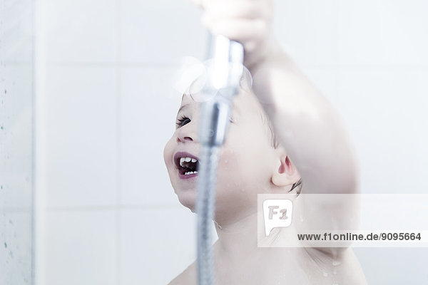 Kleiner Junge spielt mit Duschkopf im Bad