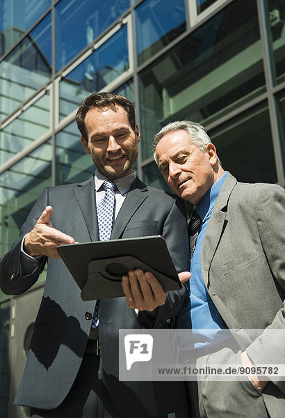 Two businessmen with digital tablet outside office building