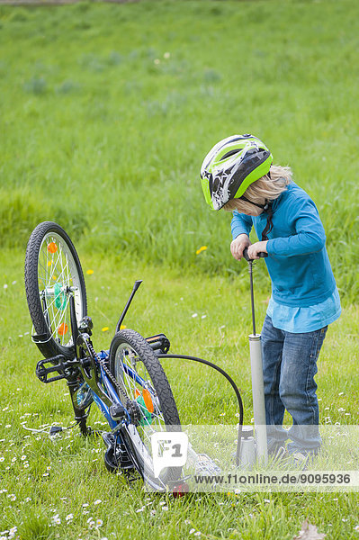 Little boy inflating bicycle tire on a meadow