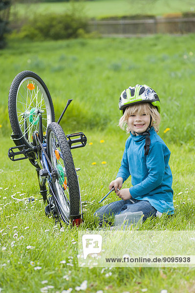 Portrait of smiling little boy repairing bicycle on meadow