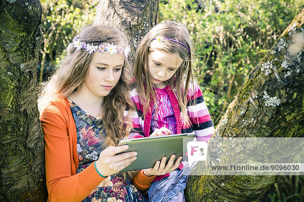 Zwei Schwestern mit Tablet-Computer zusammen im Garten
