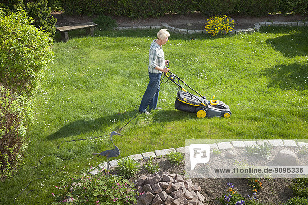 Germany  Woman mowing lawn in garden