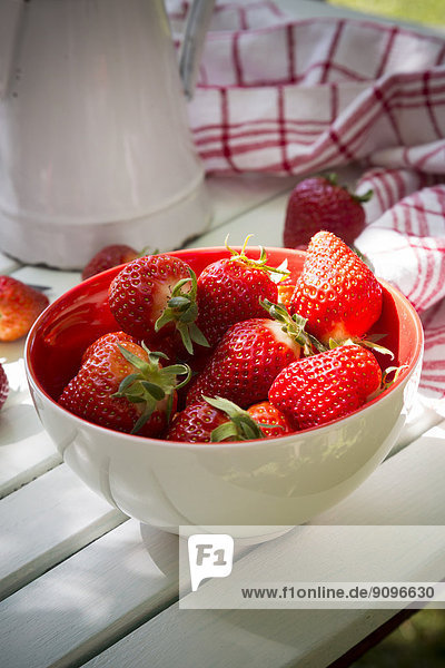 Bowl of strawberries  kitchen towel and jar on white wood