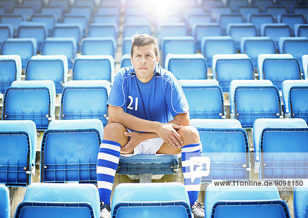 Fußballer sitzt im leeren Stadion