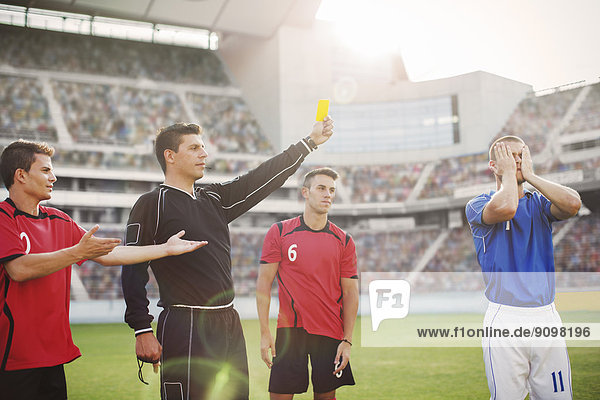 Referee flashing yellow card at soccer player on field