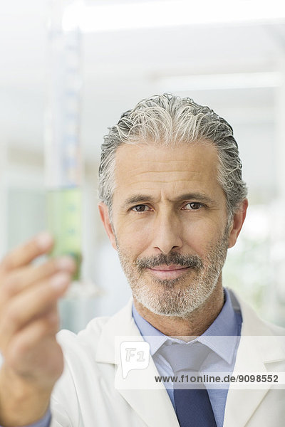 Portrait of confident scientist holding tube with green liquid