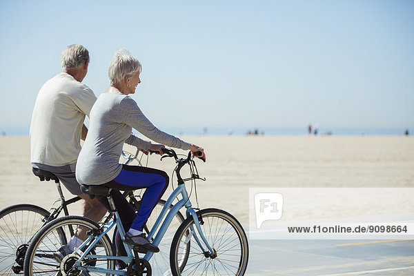 Senior couple riding bicycles on beach