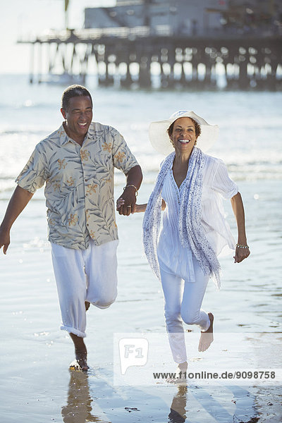 Lächelndes Seniorenpaar rennt am sonnigen Strand