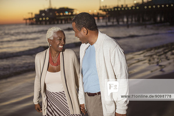 Seniorenpaar  das bei Sonnenuntergang am Strand spazieren geht