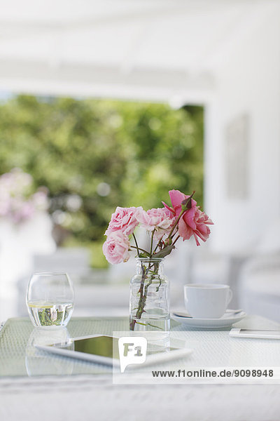 Rosa Rosen auf Terrassentisch neben Kaffeetasse und digitalem Tablett