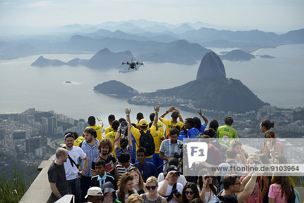 People cheering in the direction of a drone with cameras  Octopoter  on the observation deck in front of the Christ the Redeemer statue  Cristo Redentor  on Corcovado Mountain  Rio de Janeiro  Rio de Janeiro State  Brazil