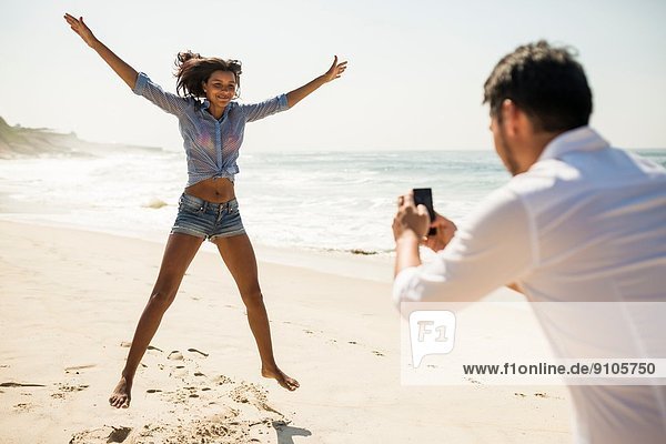 Mid adult man photographing girlfriend jumping  Arpoador beach  Rio De Janeiro  Brazil