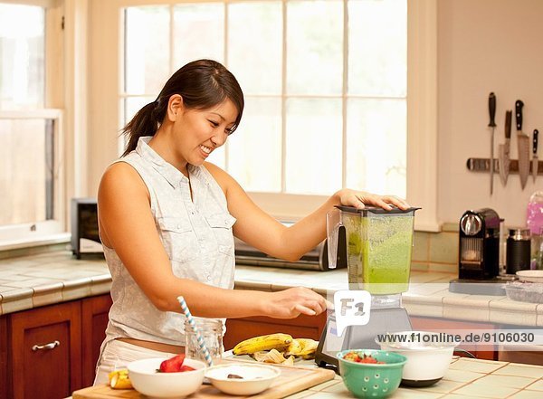 Junge Frau macht grünen Smoothie in der Küche