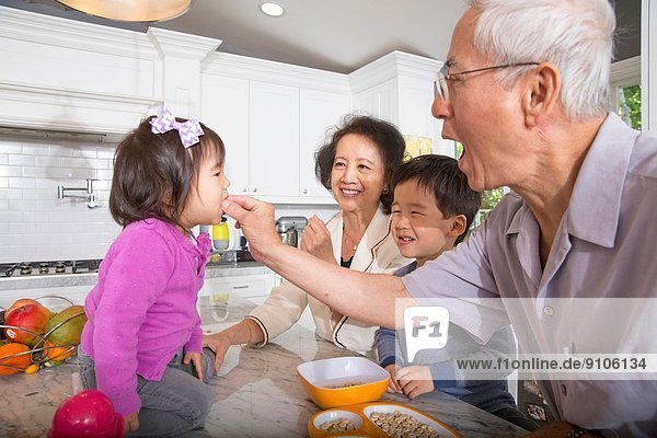 Grandfather feeding snack to toddler granddaughter in kitchen