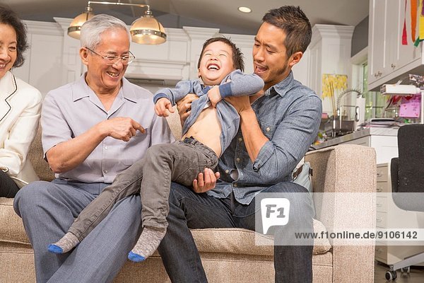 Drei Generationen Familie spielt mit dem kleinen Jungen auf dem Sofa