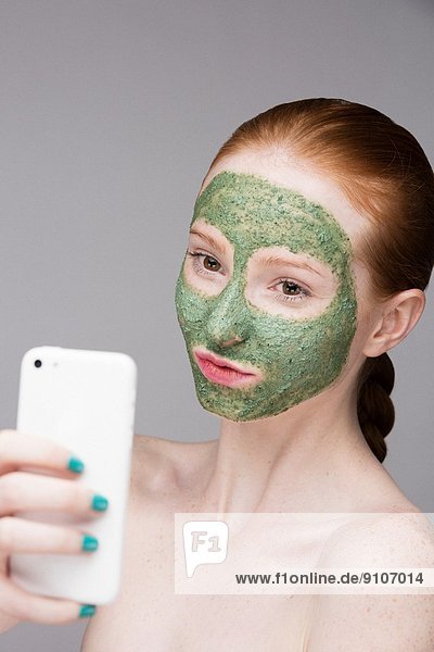 Junge Frau mit Gesichtsmaske  Selbstporträtfotografie mit Smartphone