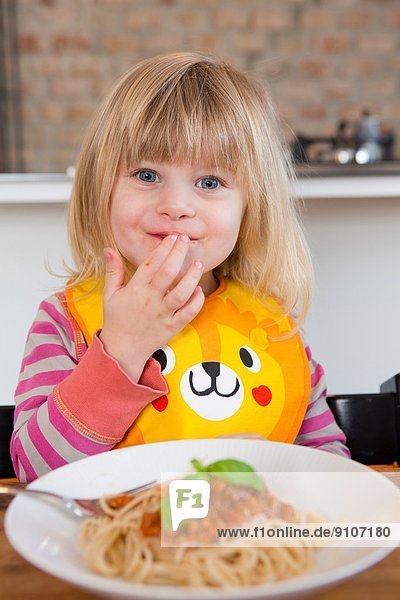 Porträt eines 2-jährigen Mädchens  das Spaghetti mit Fingern isst.