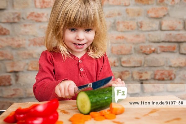 Zweijähriges Mädchen in der Küche lernt Gemüse zu schneiden