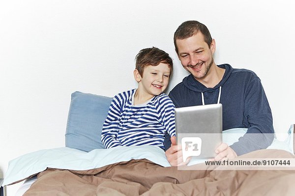 Vater und Sohn mit digitalem Tablett im Bett