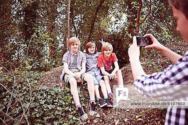 Junge fotografiert Freunde mit Telefon im Wald