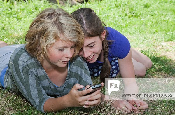 Teenage girls lying on grass  using smartphone